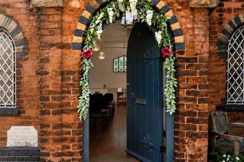 The open blue door of the chapel, decorated with a floral arch, looking through to the seating inside