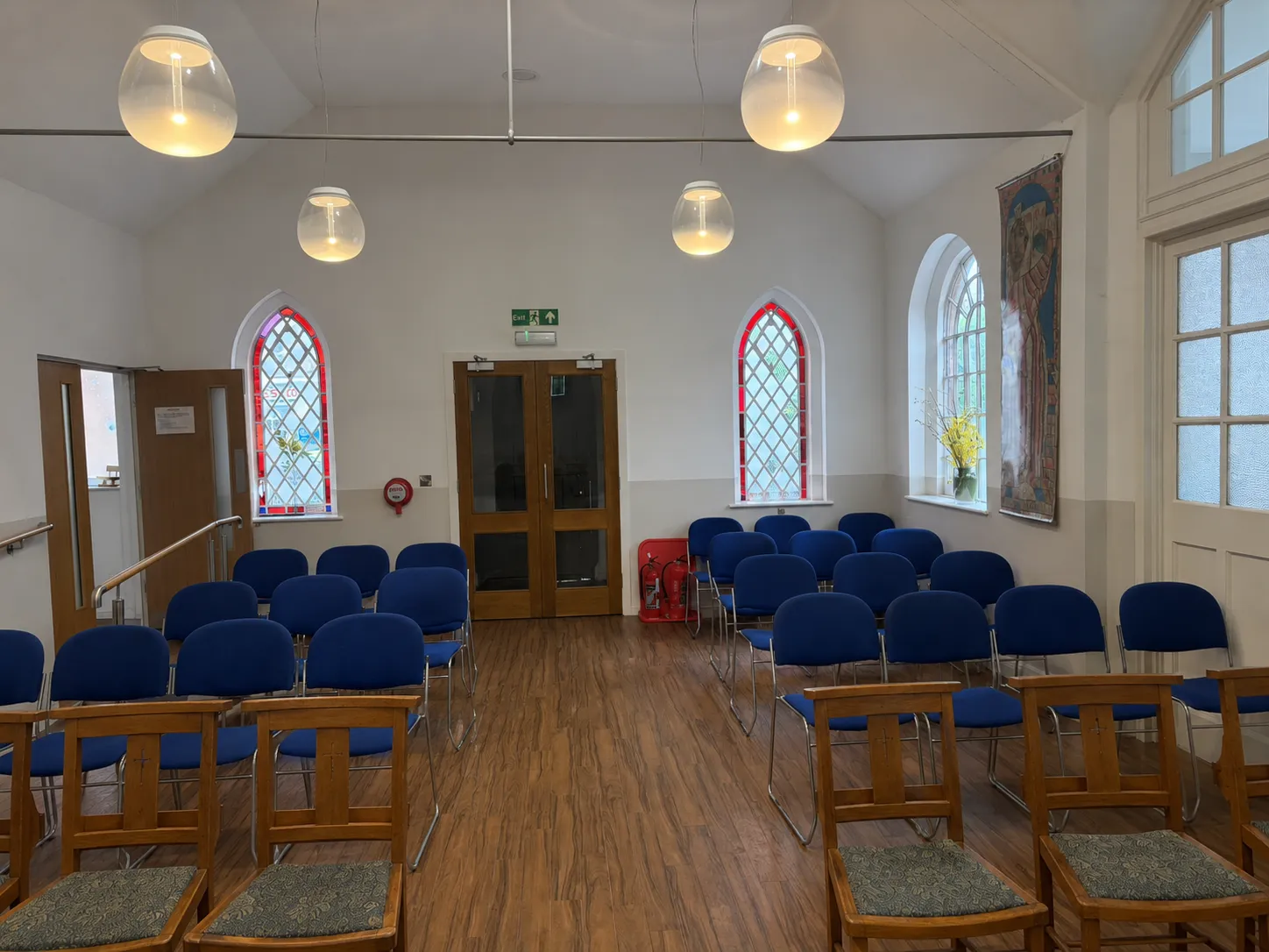 Rows of blue chairs set out in the church room, with stained-glass windows either side