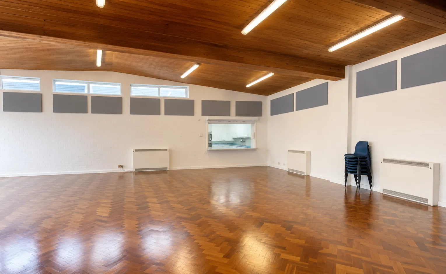 A wider view across the main hall toward the servery hatch and stacked chairs