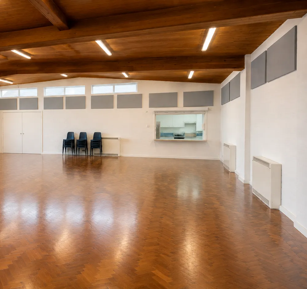 The empty main hall with its parquet floor, vaulted timber ceiling and stacked chairs against the wall