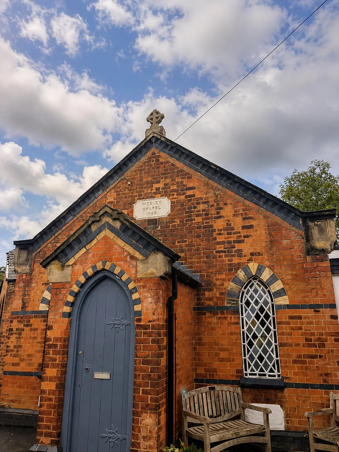 The red-brick gable end of Wesley Chapel, built in 1868, with its arched doorway and stained-glass window